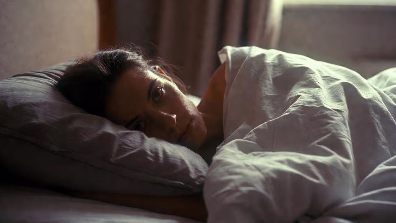Adult lying awake in bed appearing physically exhausted